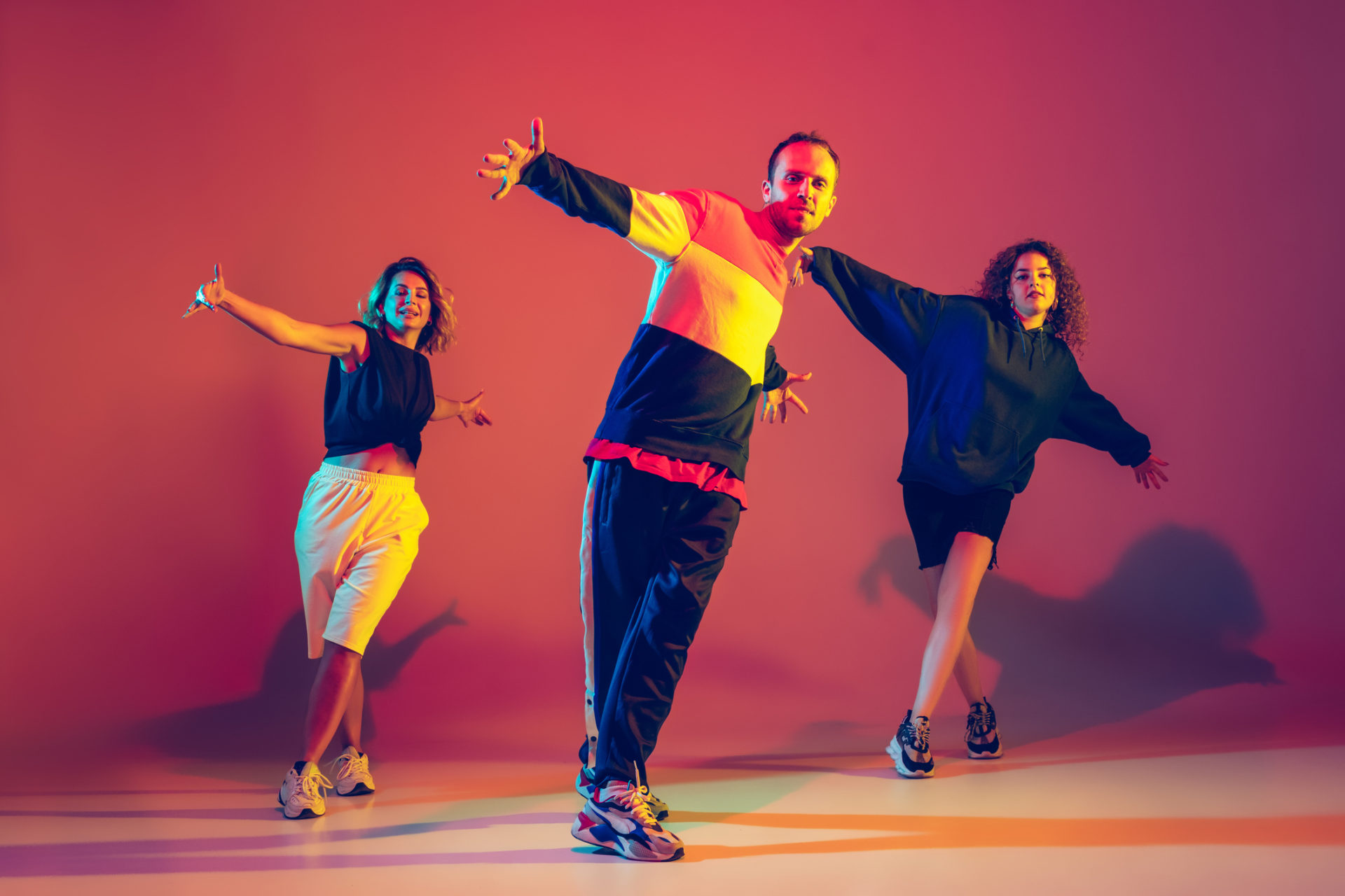 Dynamic. Stylish men and woman dancing hip-hop in bright clothes on green background at dance hall in neon light. Youth culture, movement, style and fashion, action. Fashionable portrait.